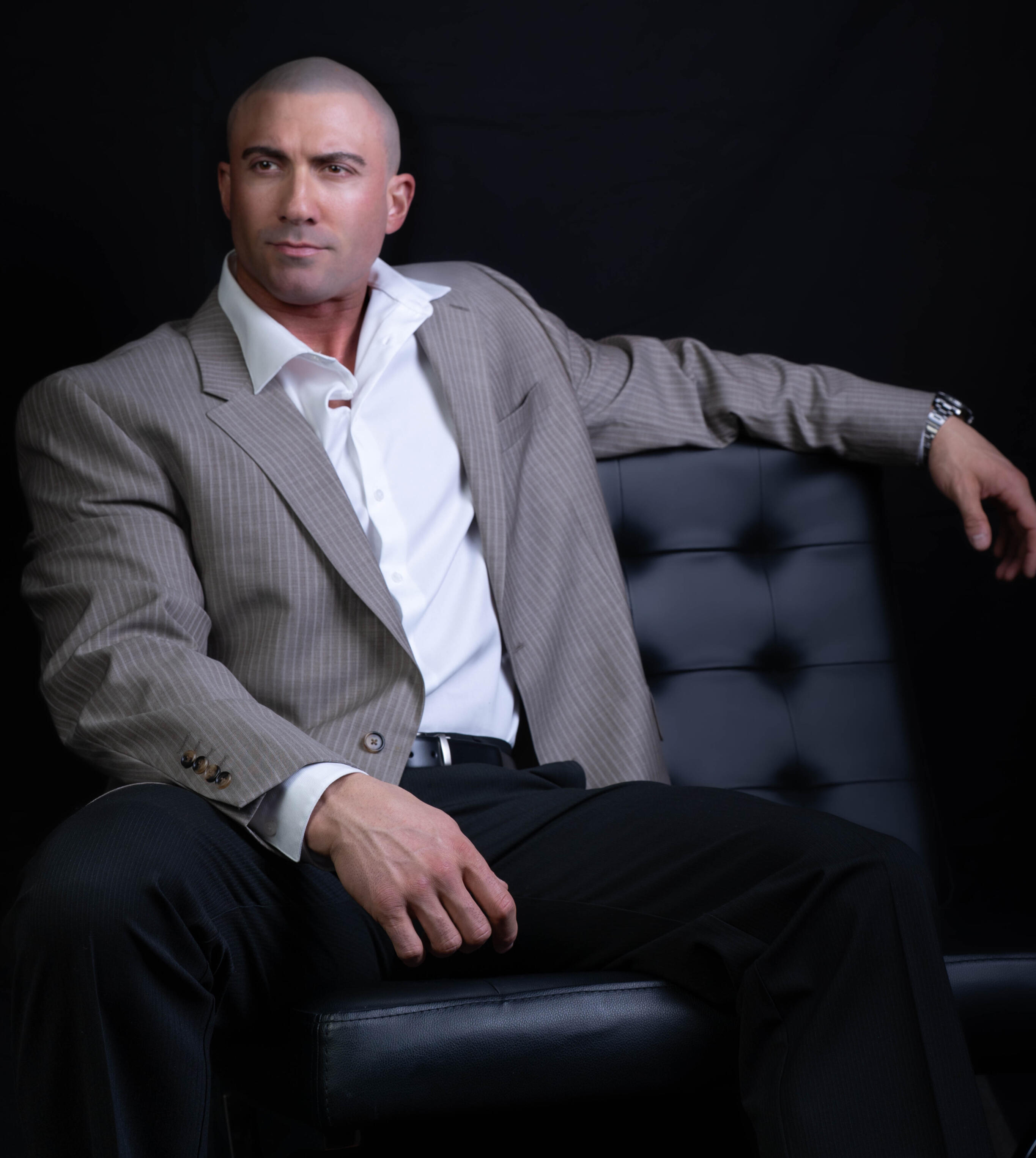 Professional photo of Thomas Rooney - performer, author, and entrepreneur wearing a suit, sitting in a Barcelona chair